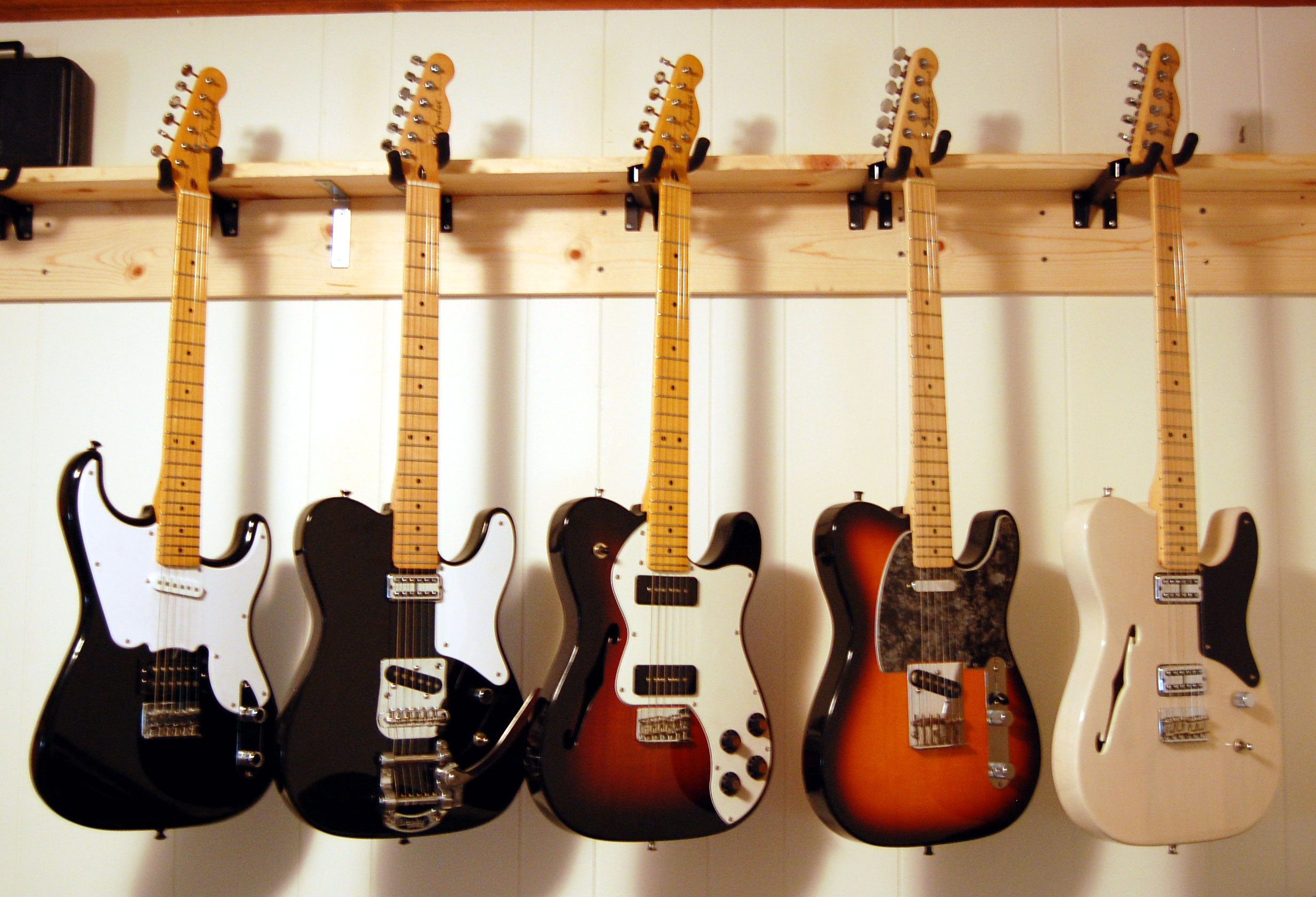 Five modern Fender Telecaster variants hanging on a wall, including Thinline and Cabronita models