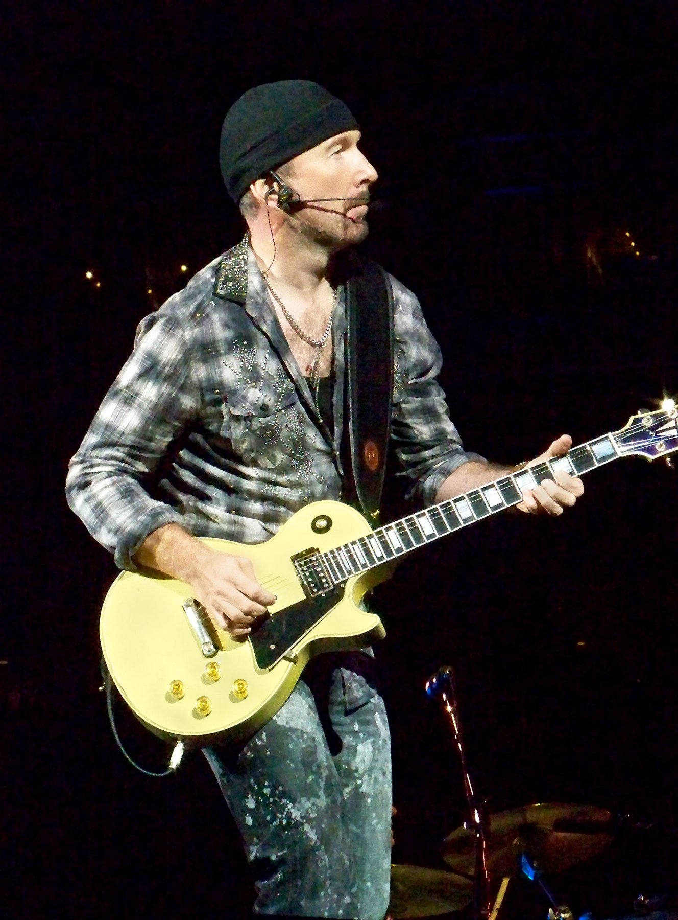 The Edge playing guitar on a stadium stage