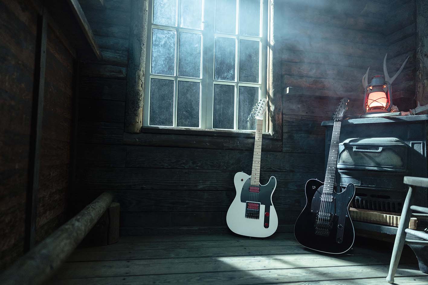 Fender John 5 Ghost Telecaster in Arctic White and John 5 Phantom Telecaster in black leaning in a dim wooden cabin