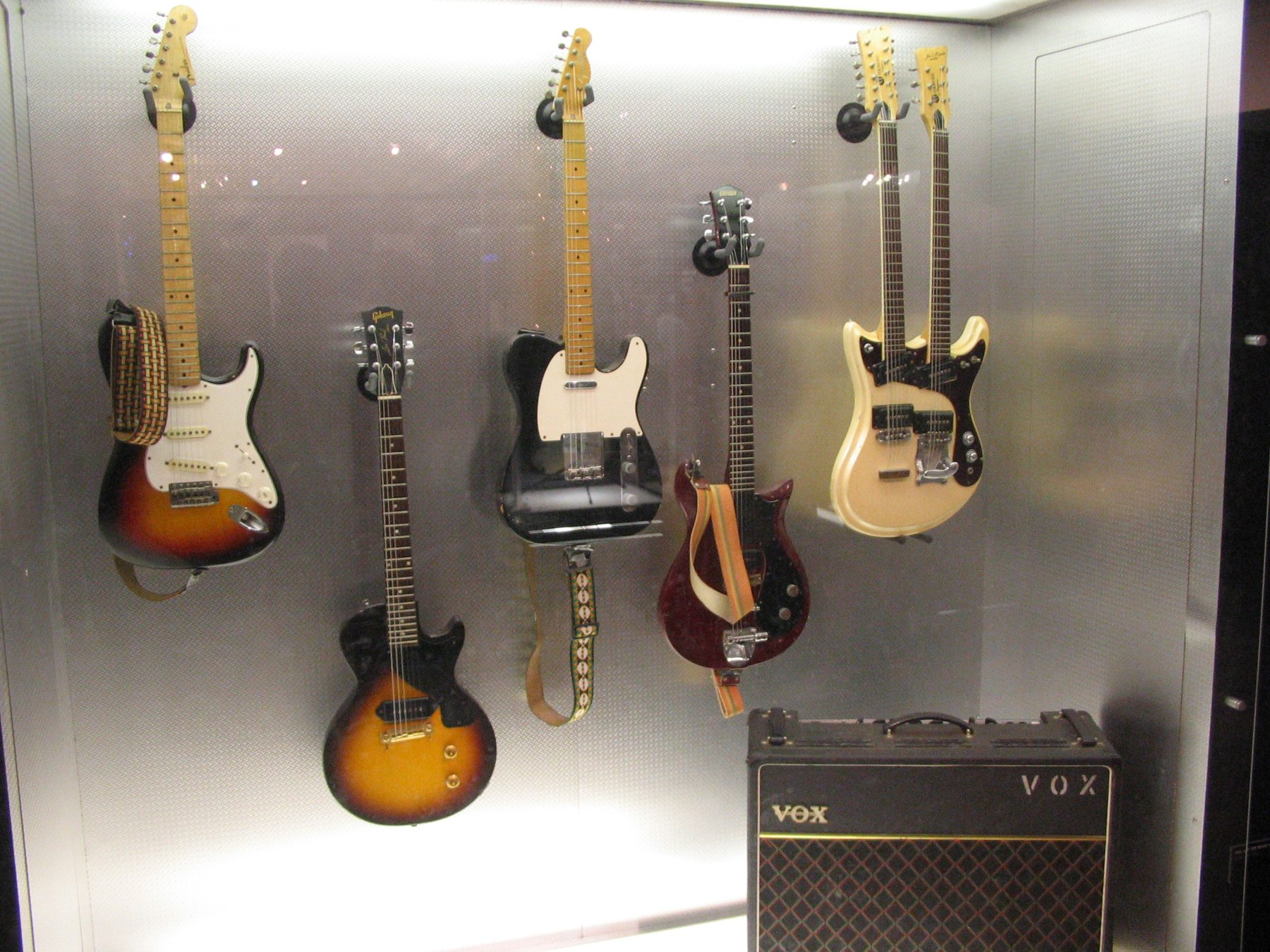 Vox AC30 amp below a wall of vintage guitars in a display case