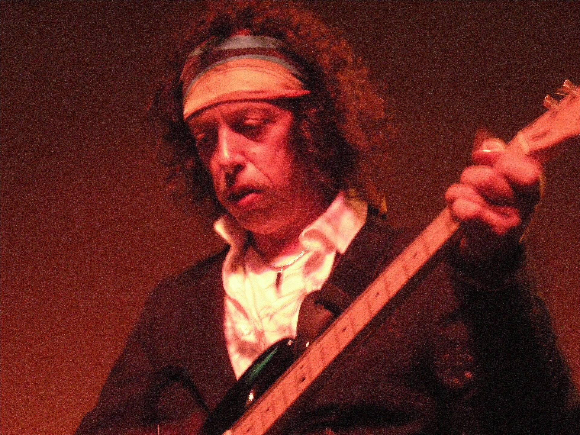 Randy Hansen in a headband playing guitar under red stage light