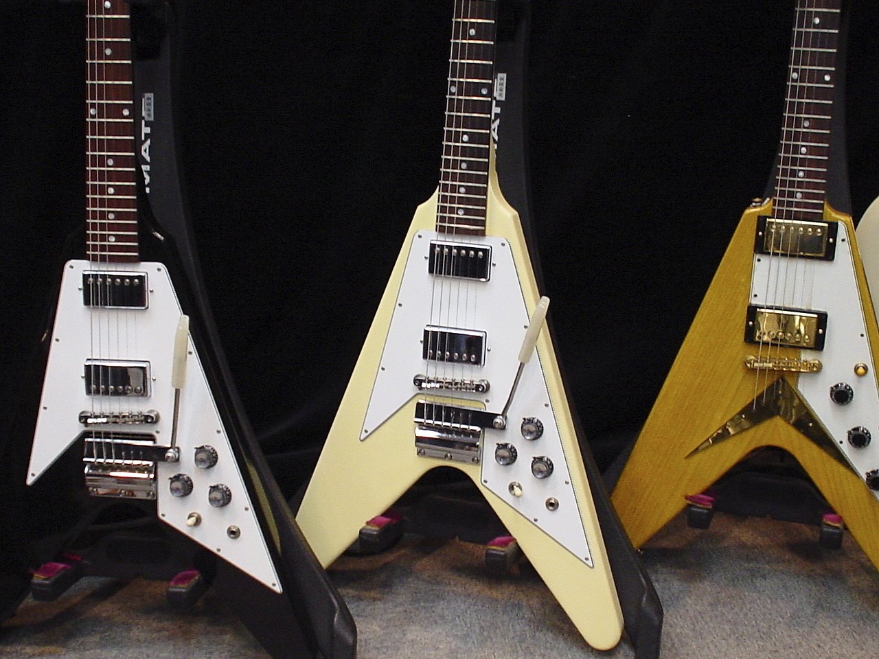 Three Gibson Flying V electric guitars in black, white and natural finishes standing side by side
