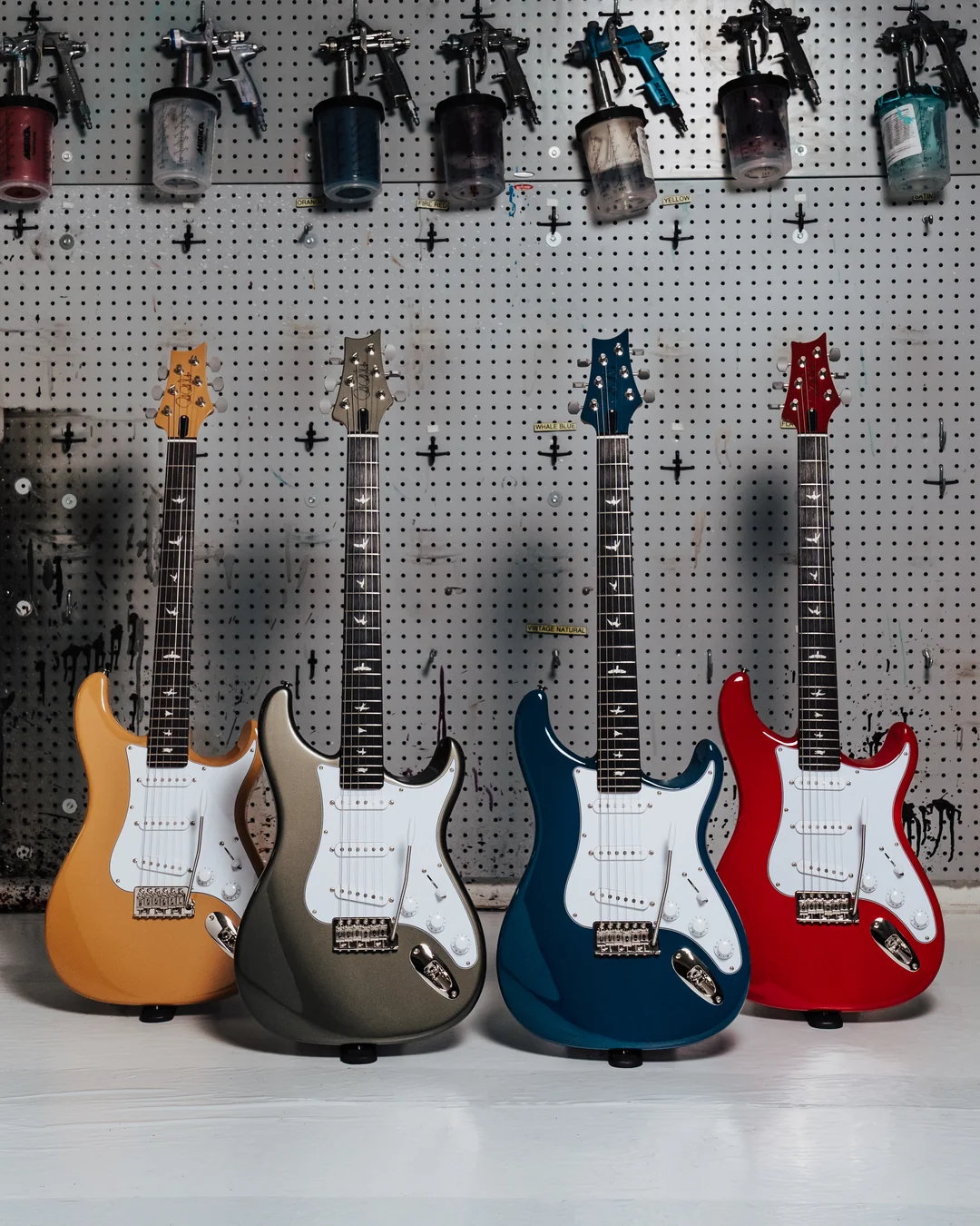 Four PRS Silver Sky guitars in yellow, gray, blue and red finishes in a guitar workshop