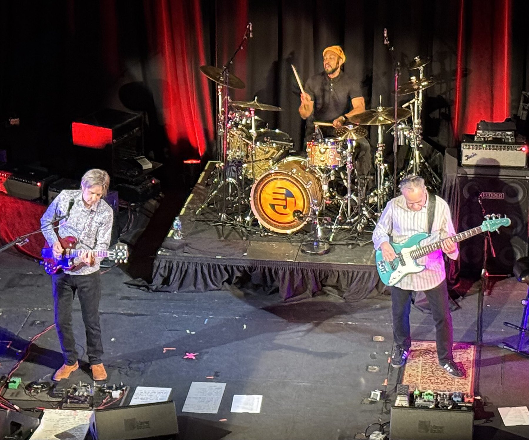 Eric Johnson playing a red guitar at the front of the stage with his drummer and bassist at the Colonial Theatre in Phoenixville, Pennsylvania, October 2025