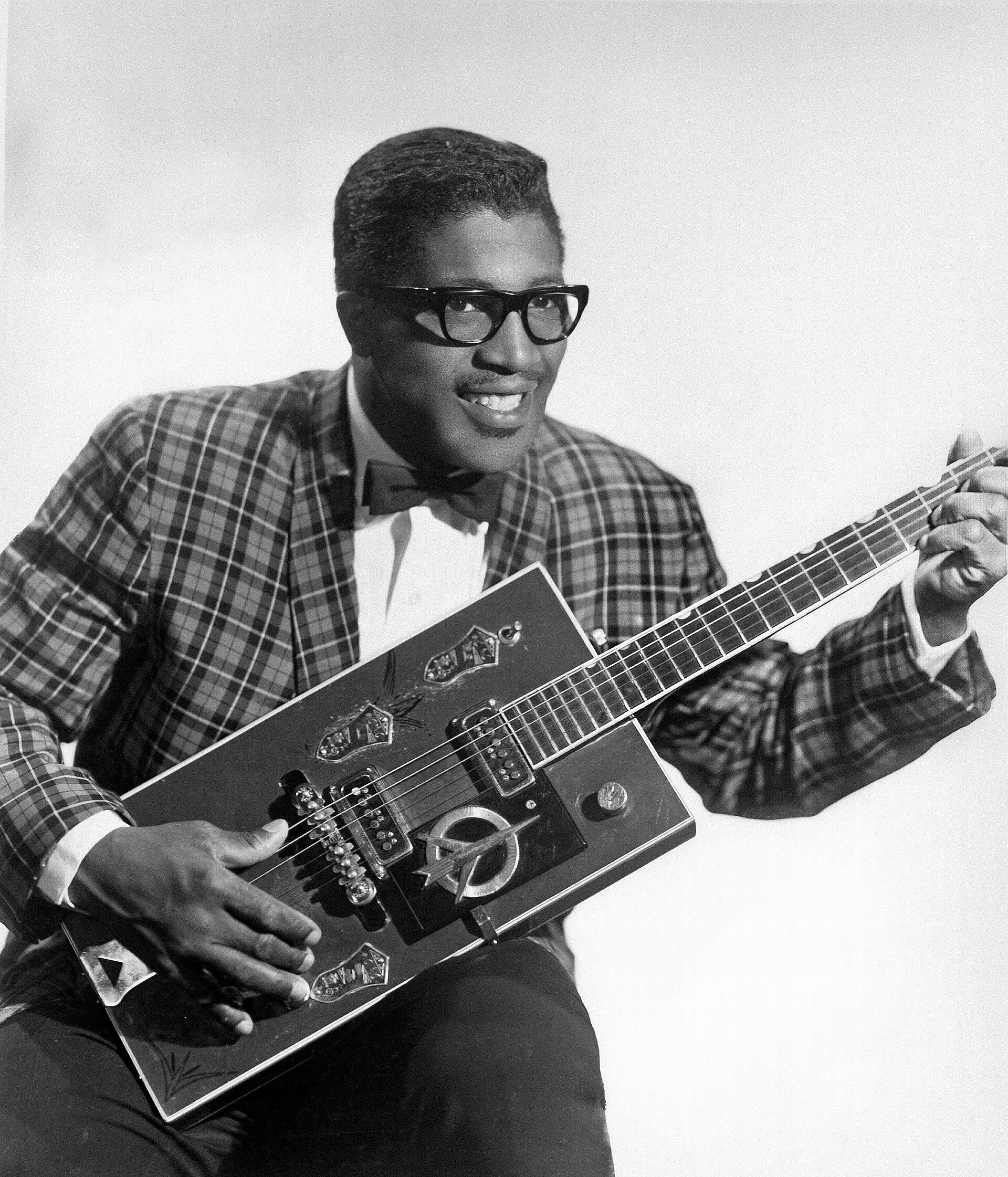 Bo Diddley in a 1957 Chess Records publicity portrait, seated and smiling with his rectangular Gretsch guitar