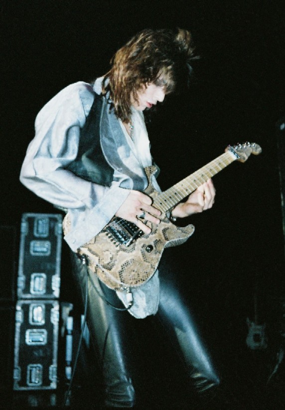 Warren DeMartini in a leather vest playing a graphic-finished guitar onstage