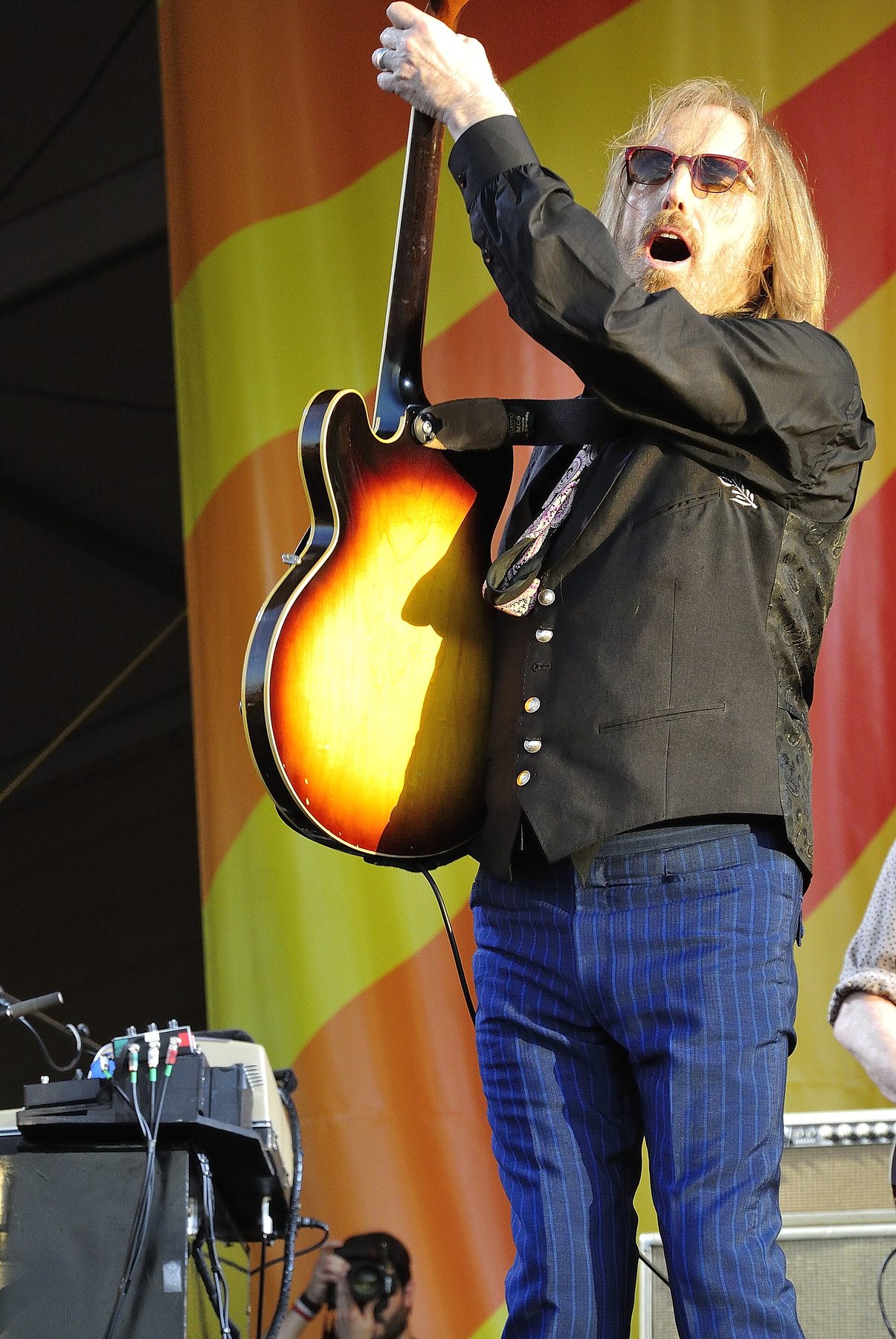 Tom Petty raising a sunburst guitar above his head on stage at the 2012 New Orleans Jazz and Heritage Festival