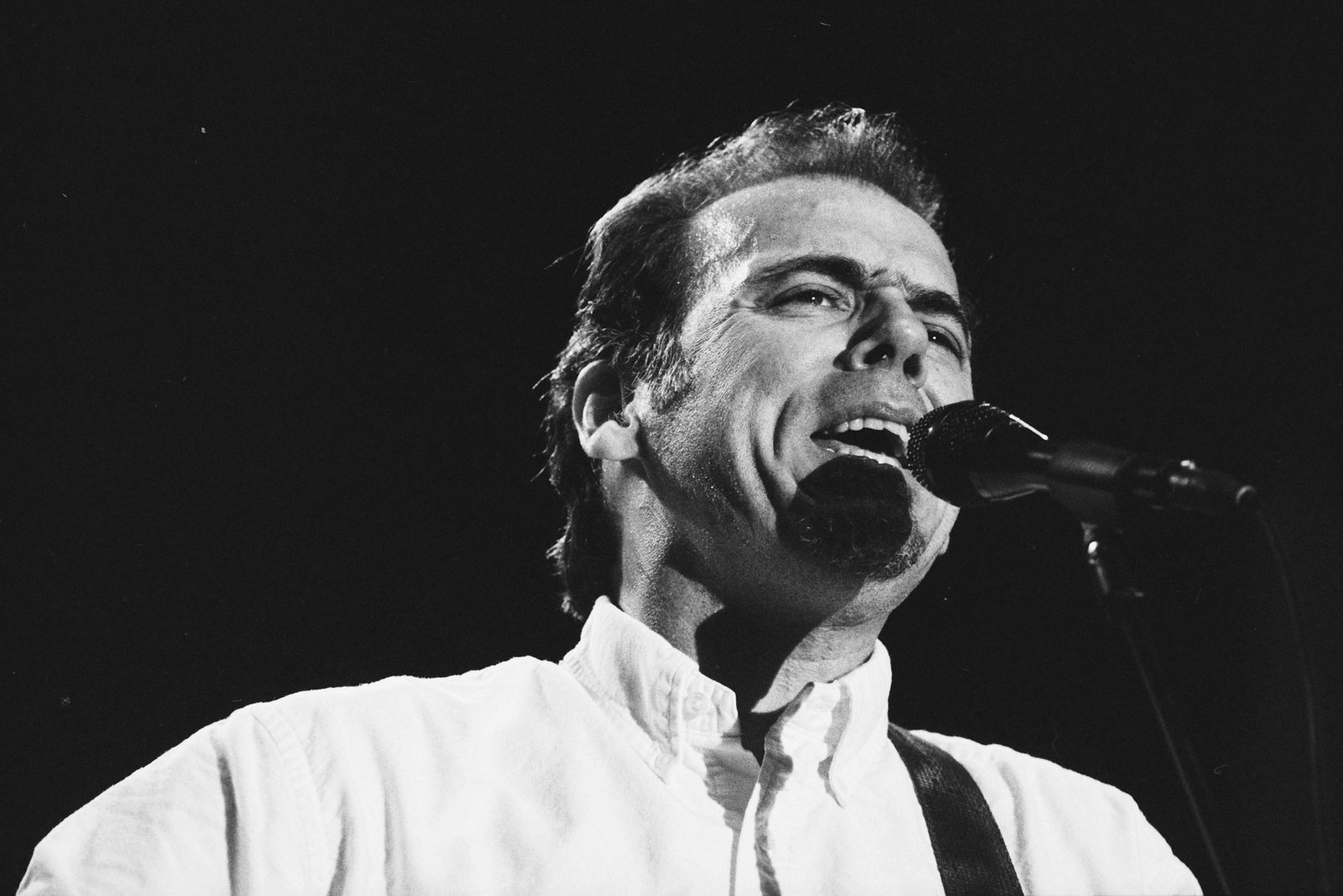 John Hiatt singing into a microphone on stage in Amsterdam in 1994