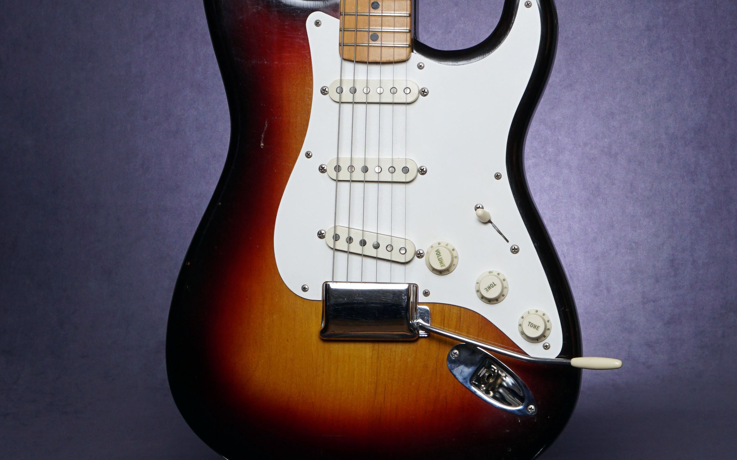 The body of a 1958 Fender Stratocaster in three-color sunburst, showing its contours, white pickguard, three single-coil pickups, control knobs and chrome bridge cover