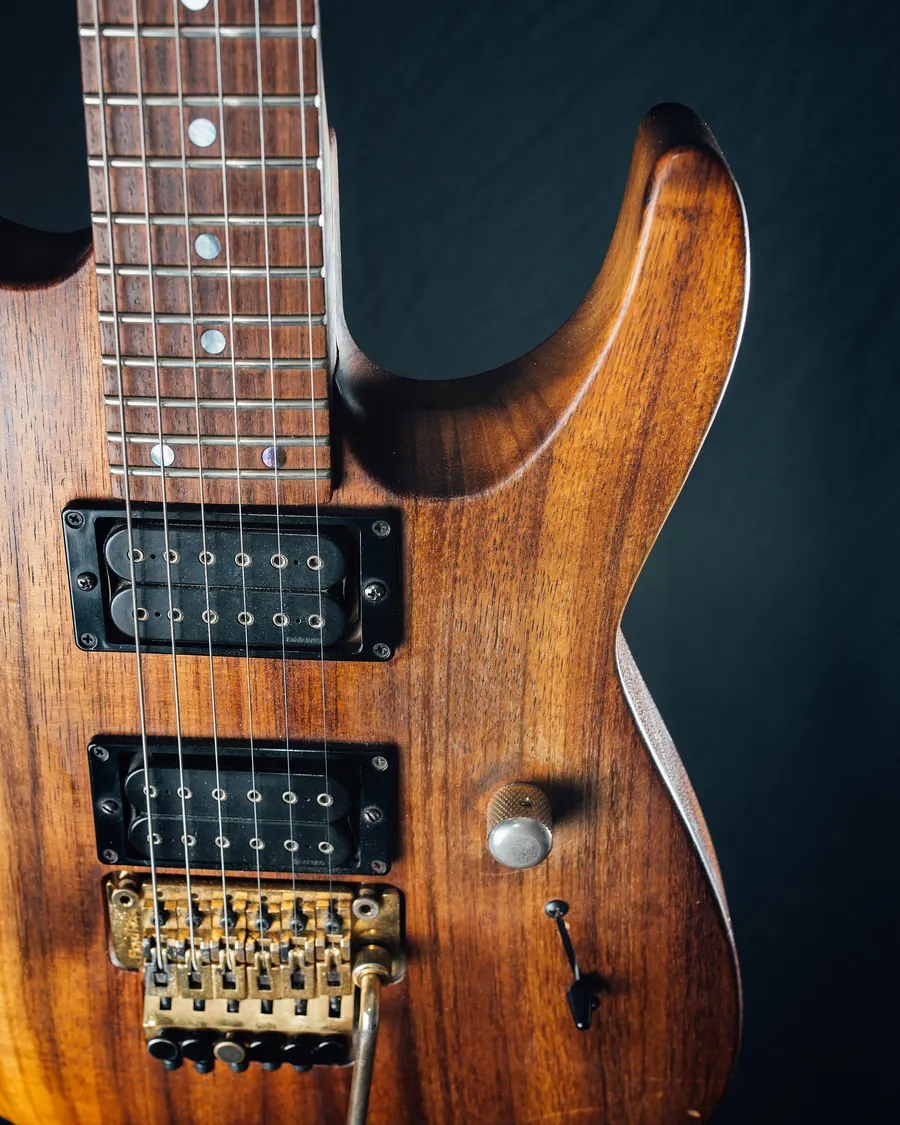 Close-up of a walnut-finish Charvel electric guitar with two humbuckers and a tremolo bridge against a black background